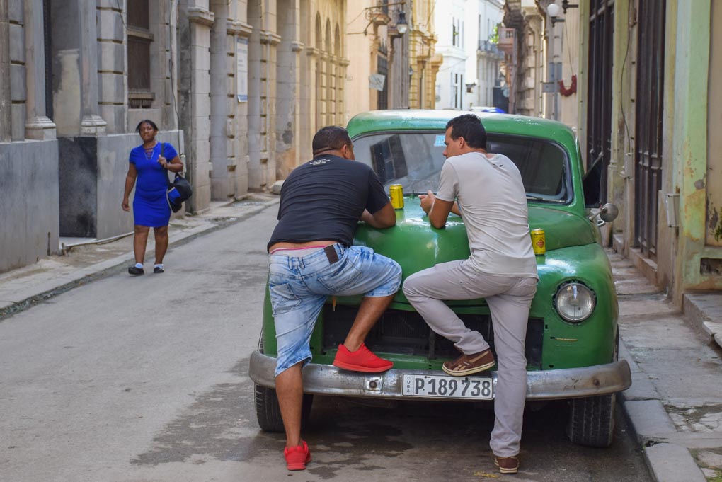 Two cuban men have a beer in downtown Havana while leaning on a car