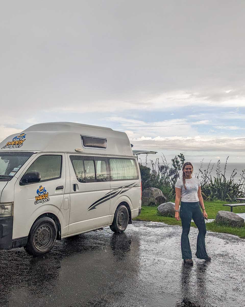 Bailey poses for a photo with her Happy Campers campervan in Raglan, New Zealand