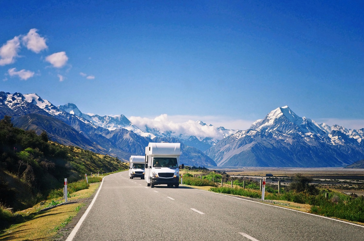 two motorhomes drive on a road towards Mount Cook in NZ on a sunny day