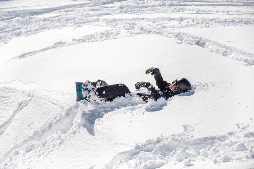 A man sits in the snow with his snowboard
