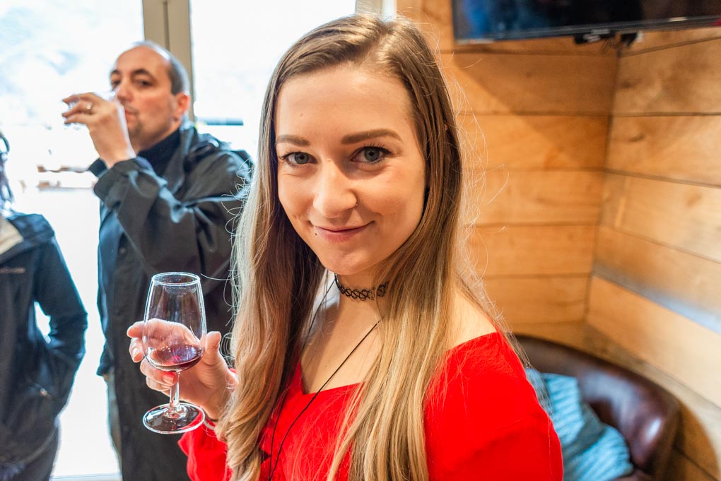 Bailey hiding her tasting glass of wine and smilling at the camera at kinross Winery near queenstown