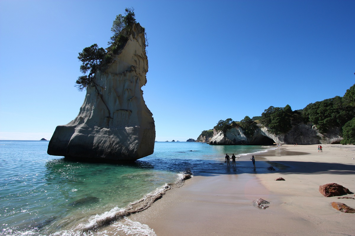 a large rock formation sticking out of the water at a beautiful beach bay next to Cathedral Cove