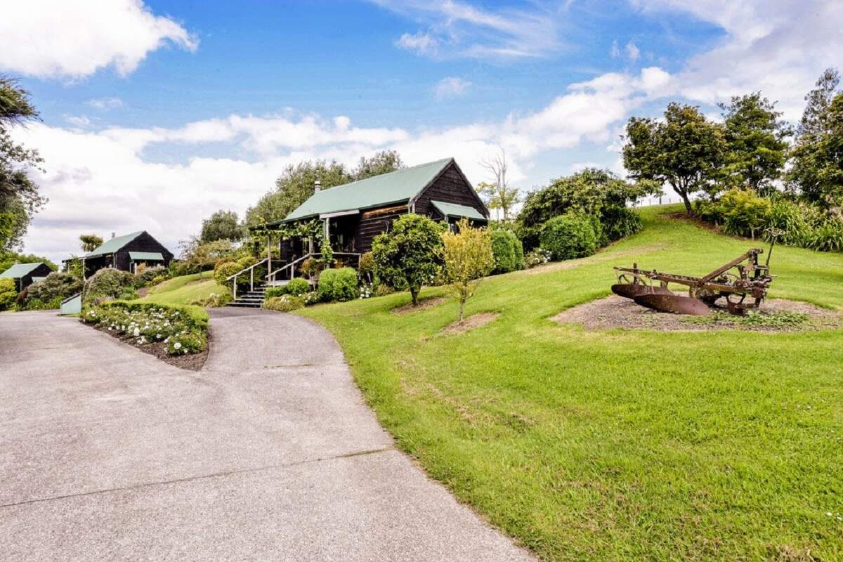 rolling green hills of grass with a small wooden cottage at Vineyard Cottages Kumeu