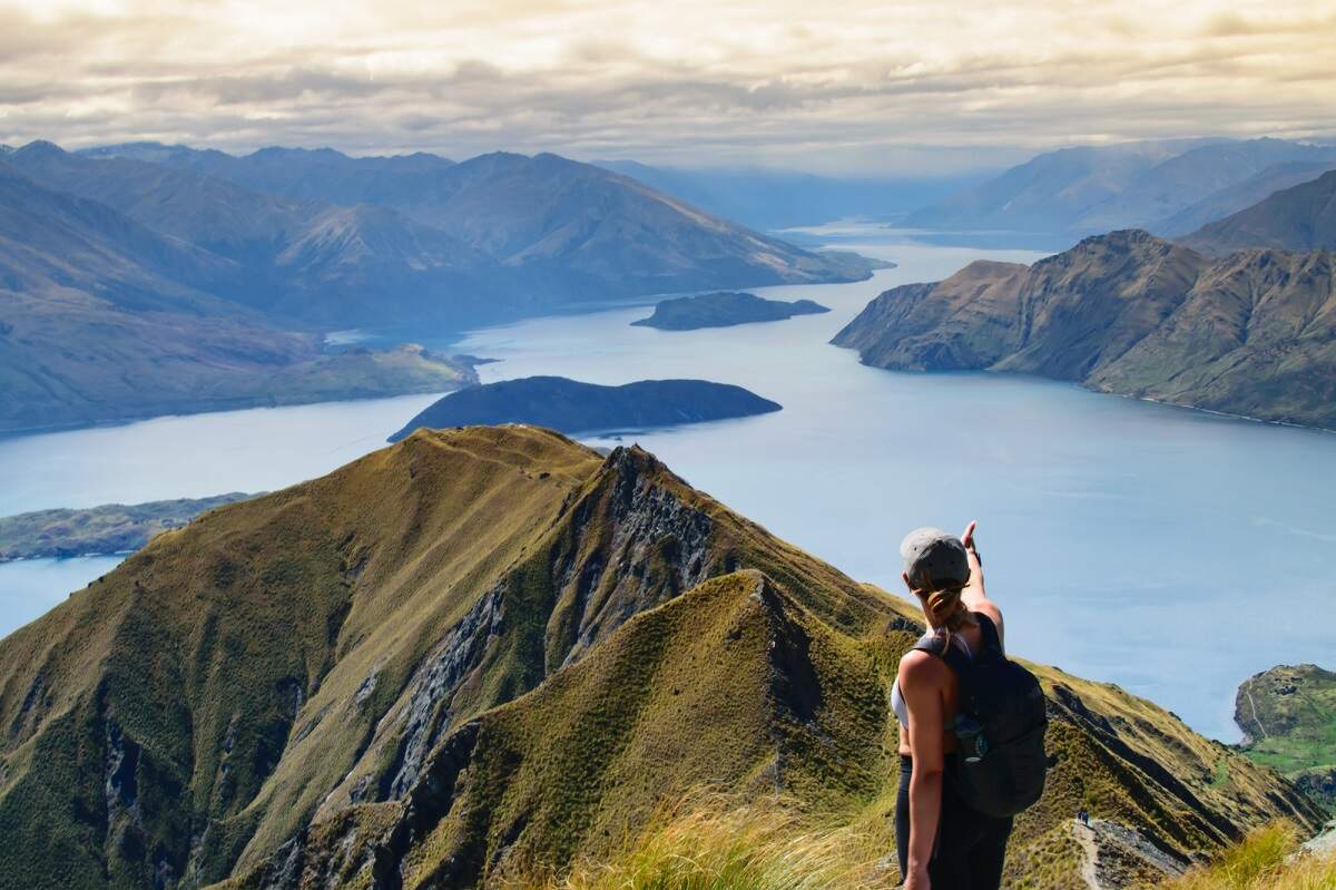 woman stands at the summit of Roys Peak in New Zealand