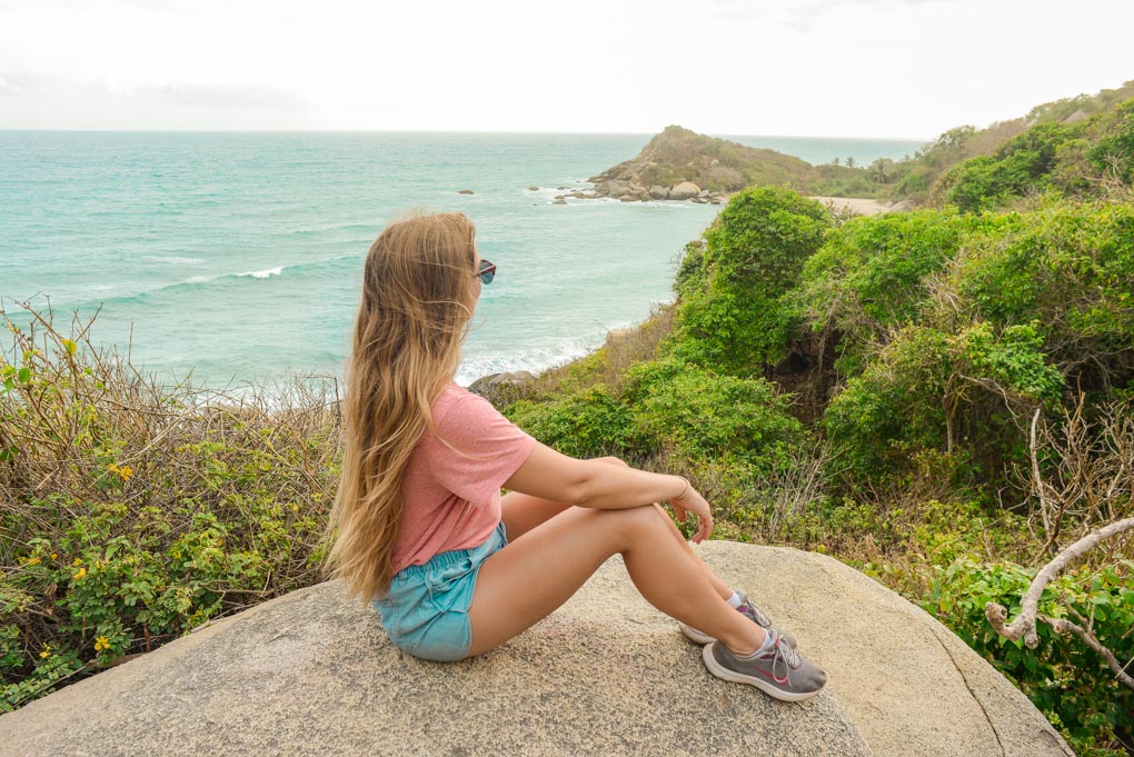 A lady sits on a rock overlooking a beach in Tayrona National Park