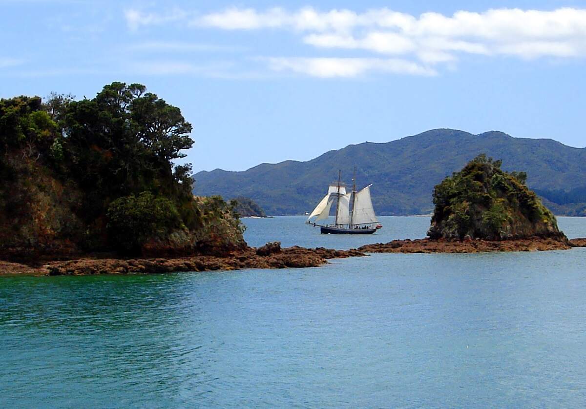the historic ship R. Tucker Thompson sailing in the distance in the Bay of Islands