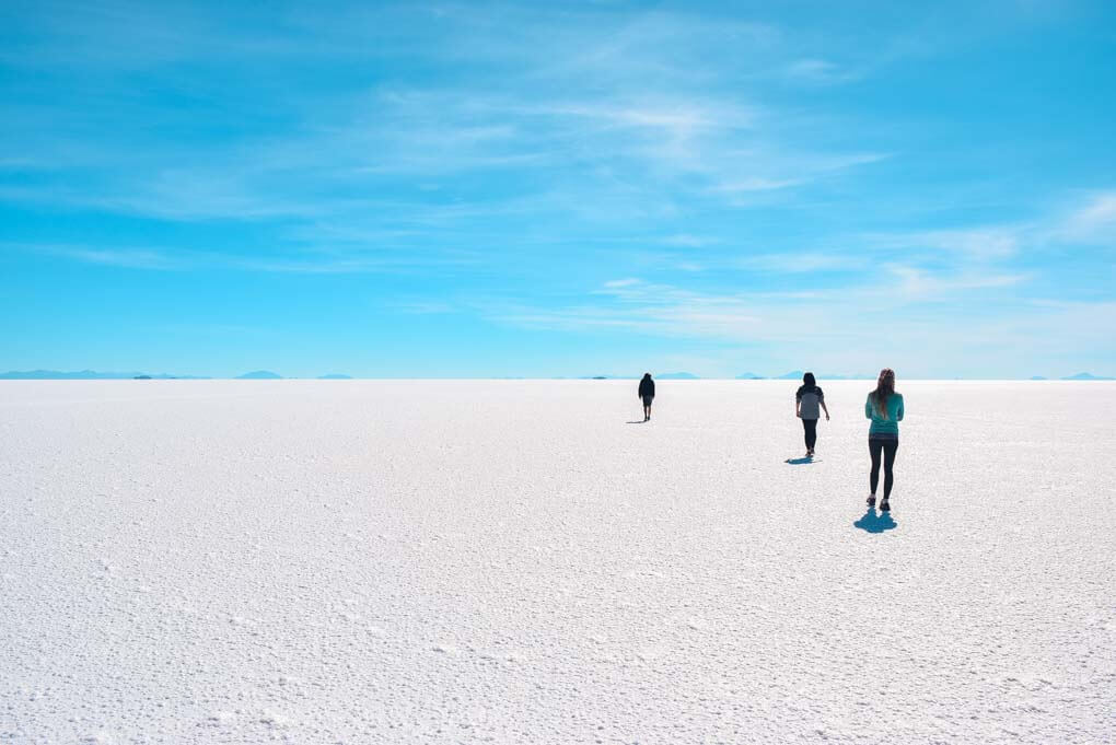 3 people walk on the salt flats in Bolivia showing just how large they are