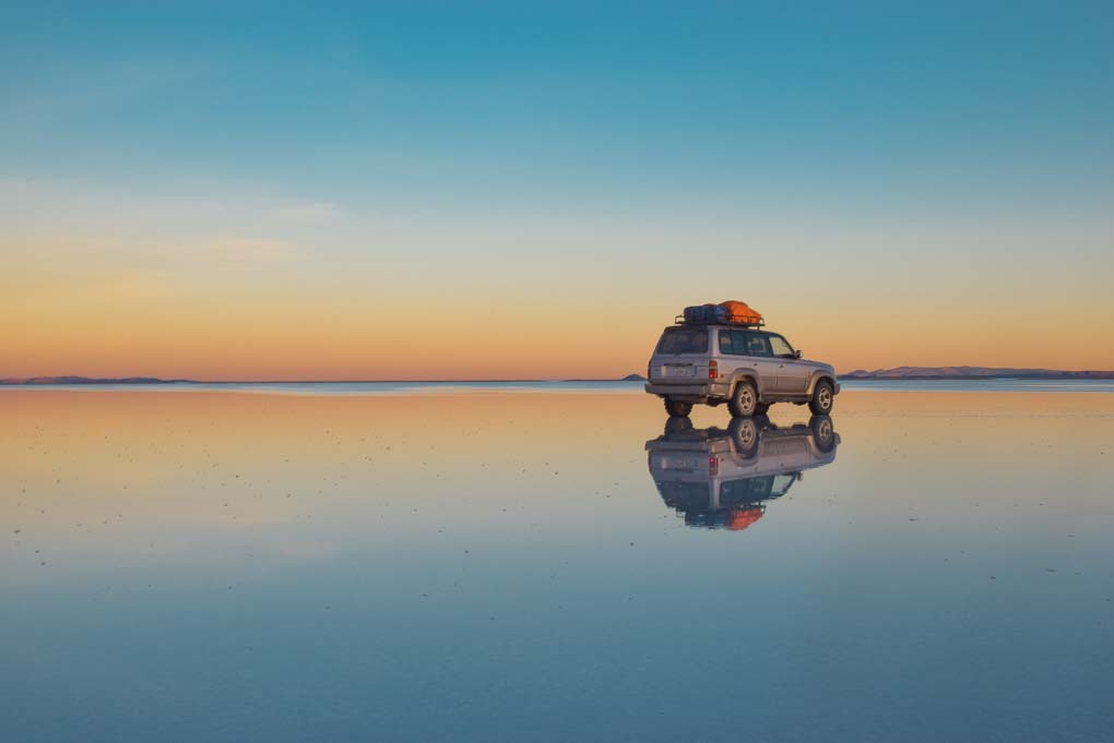 A 4wd sits in the water on the salt flats and shows how amazing the reflections are during the rain season