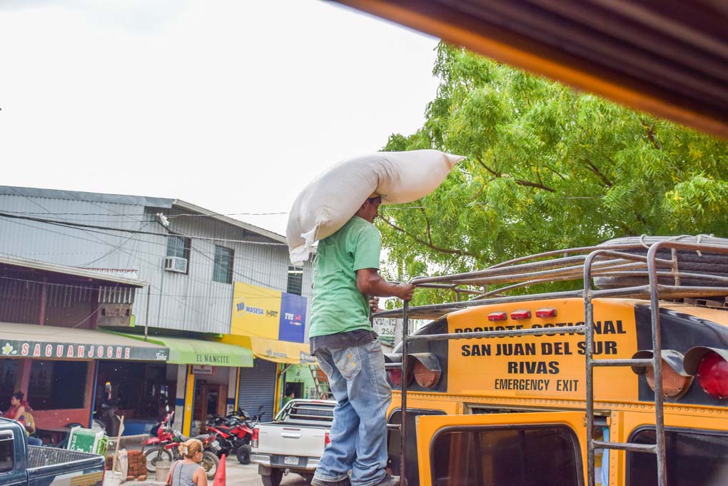 A man loads goods onto the roof of a chicken bus in Central America