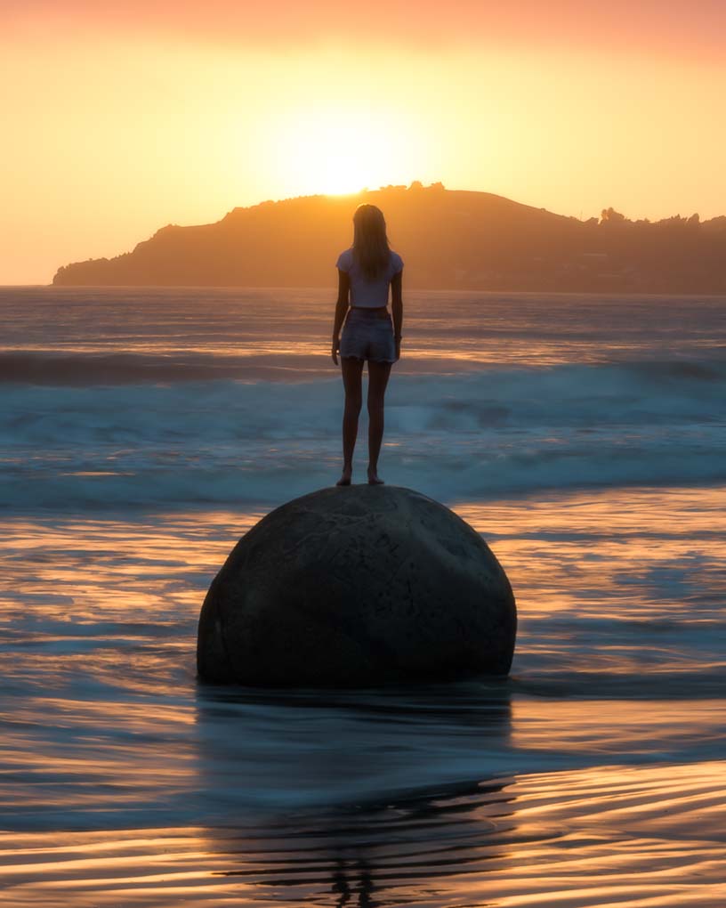 person standing on a moeraki boulder in New Zealand