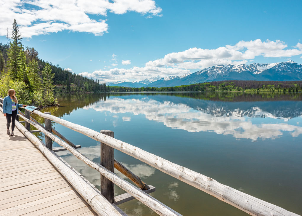A lady walks the Pyramid Island boardwalk in Jasper National park on a sunny day admiring the reflections on the lake