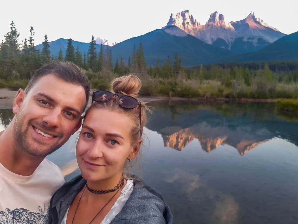 Bailey and Daniel take a selfie with the Three Sisters Mountain Range in the background in Canmore