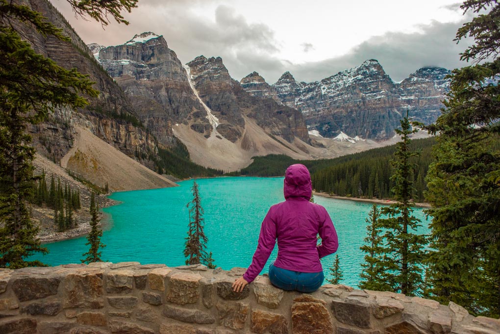 A lady sits on a rock wall at the Rockpile at Moraine Lake in Banff