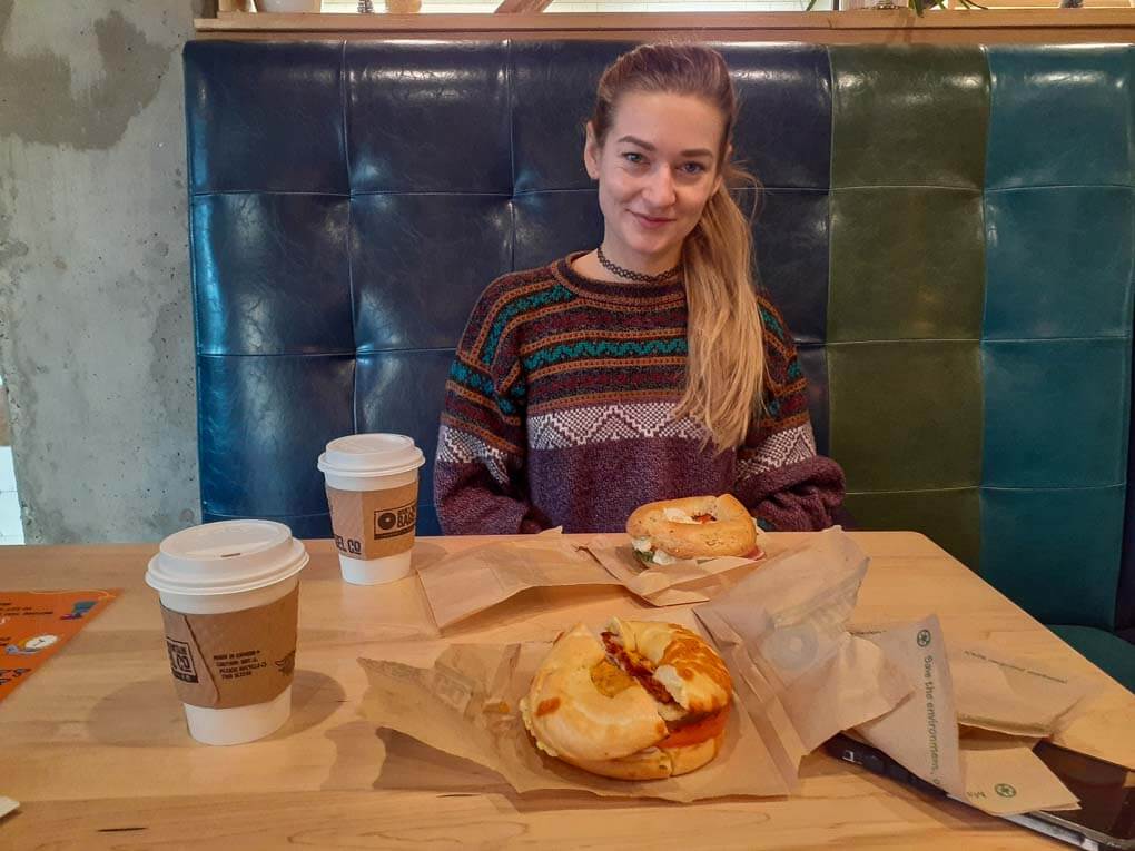 A lady poses for a photo with her bagel from Rocky Mountain Bagel Company