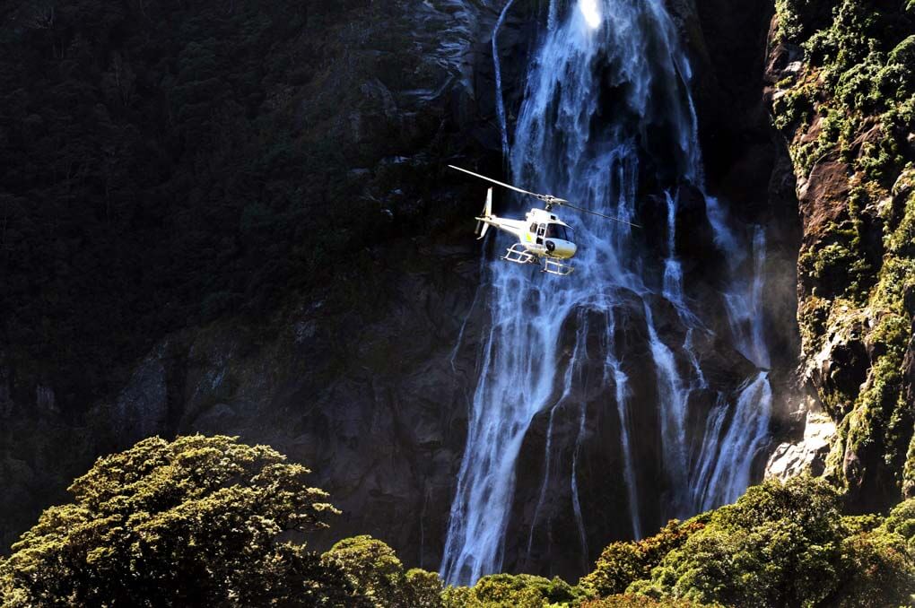 A helicopter flies though Milford Sound, New Zealand