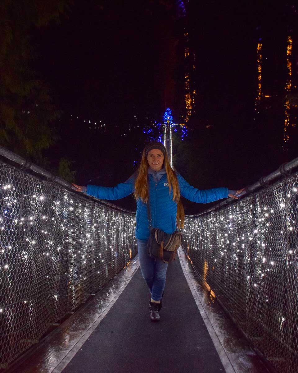 Bailey stands on the capilano suspension bridge at night surrounded by lights on a trip from Vancouver Canada