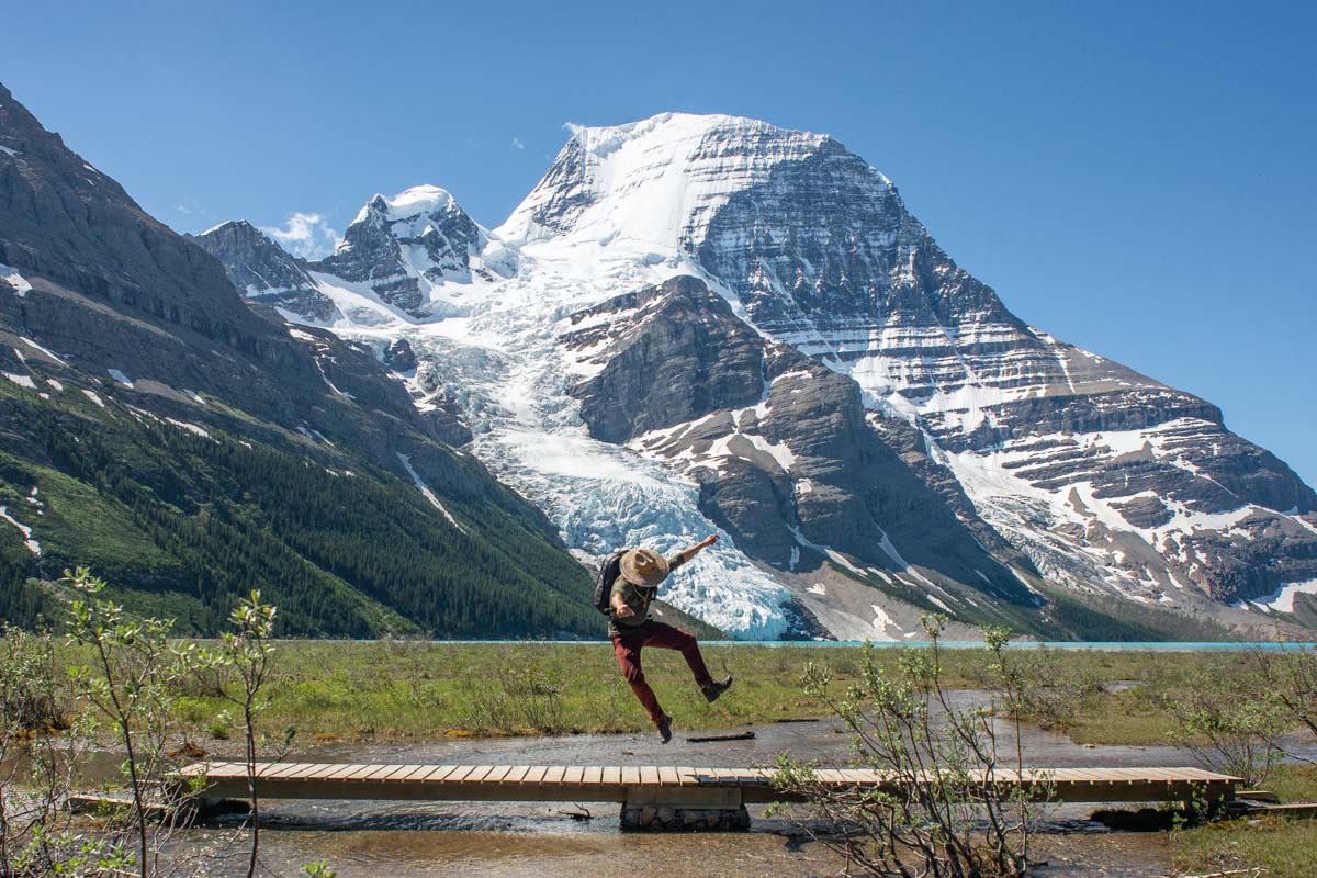 A man jumps in the air with Berg Lake and Berg Glacier in the background on the Berg LAke Trail near Valemount, BC