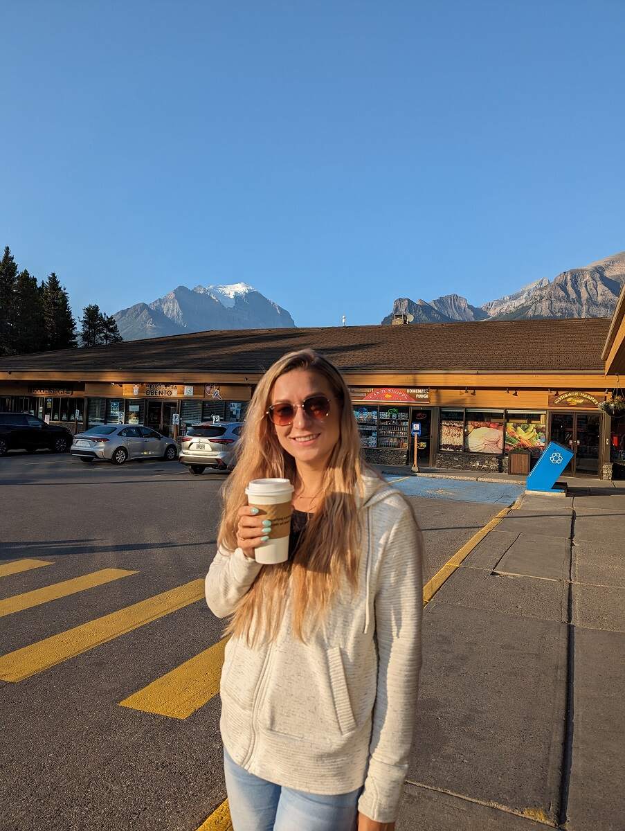 Bailey stands in a parking lot in Lake Louise with a coffee in her hand and mountains in the background