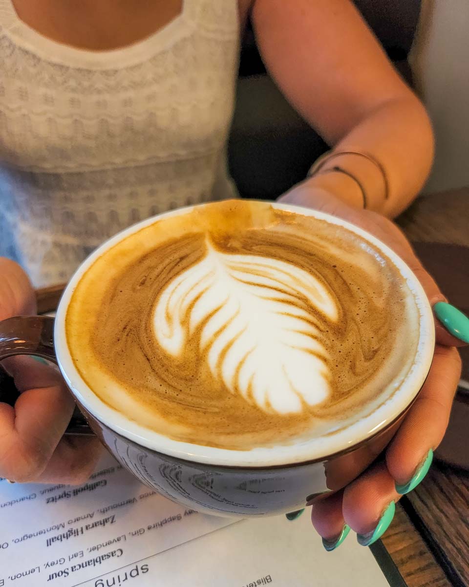 woman holds a cappuccino with a leaf on it as coffee art