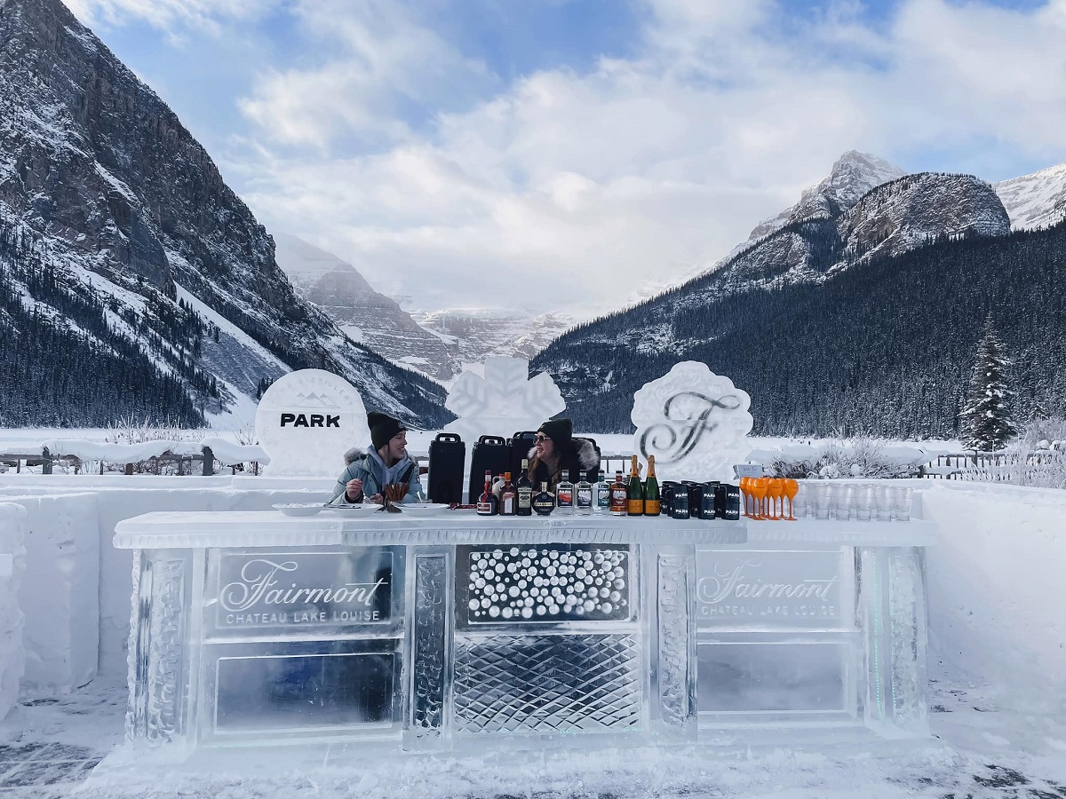 a bar carved out of ice on Lake Louise with two people sitting there ready to serve drinks