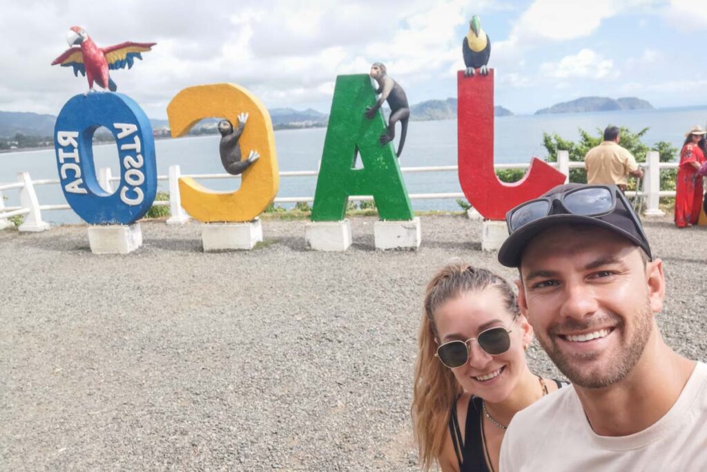 Bailey and Daniel from Destinationless Travel take a selfie with the Jaco Sign