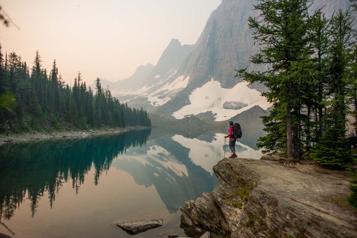 A lady stands on the edge of Floe Lake on a Smokey summer day