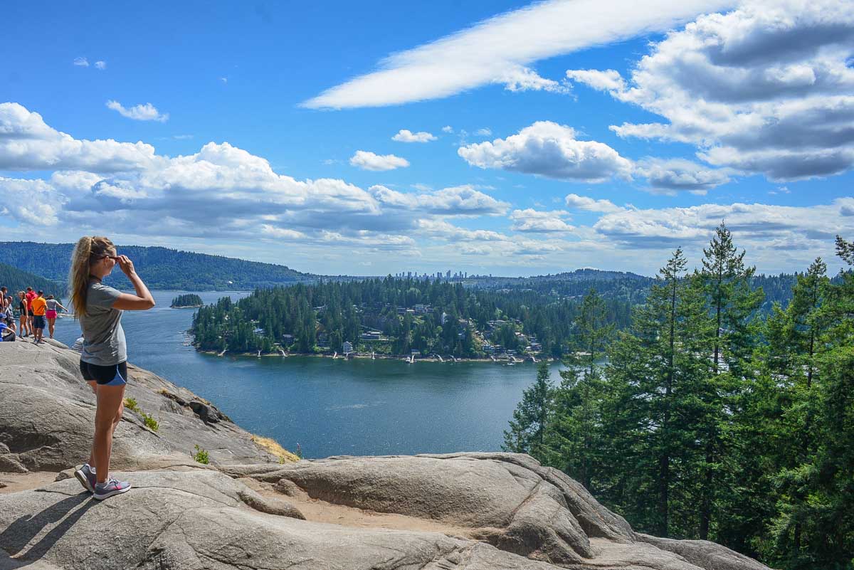 A lady stands on a rock and looks out at the view on the Quarry Rock Trail in Vancouver
