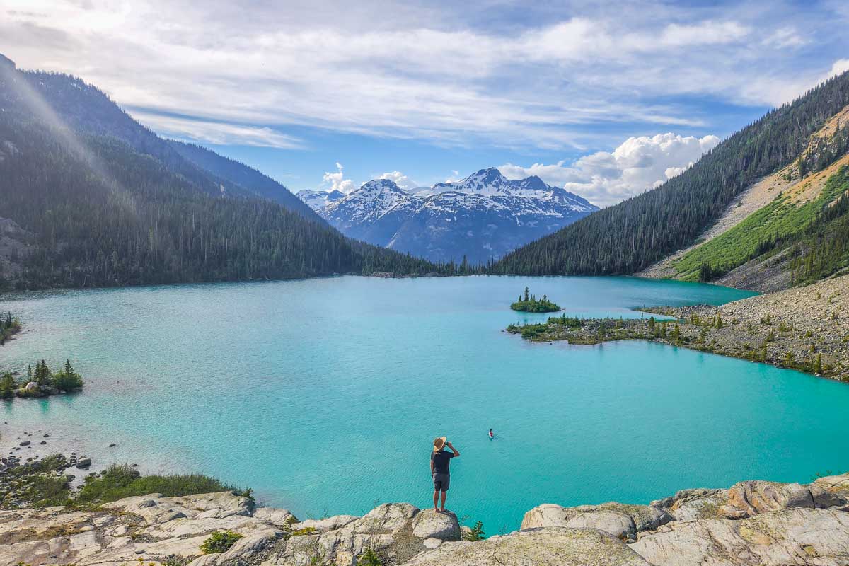 A man stands on a cliff at the very end of Joffre Lakes Trail