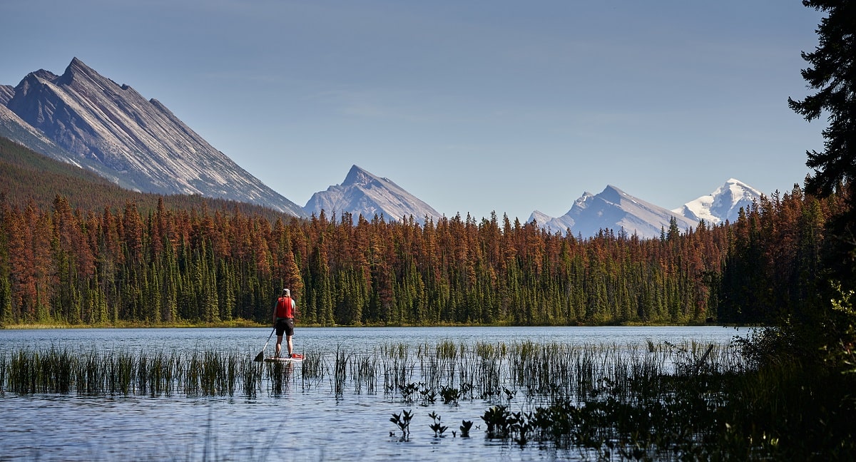 man stand-up paddleboarding on a calm lake with mountains in the background