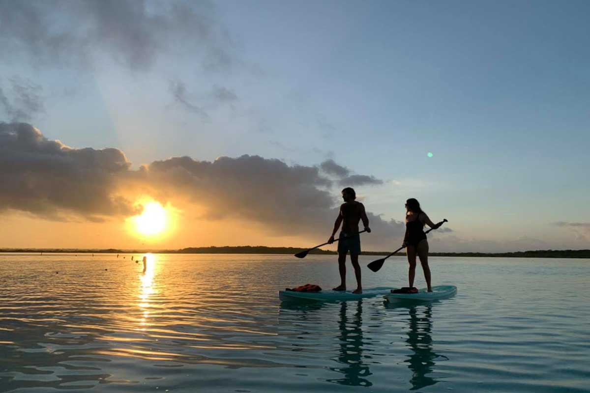 Two peopl paddleboard on Bacalar Lagoon at sunrise