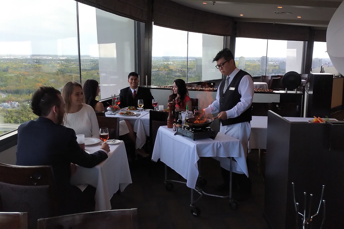 a waiter cooking infront of a table of guests with views over Edmonton River Valley in the distance