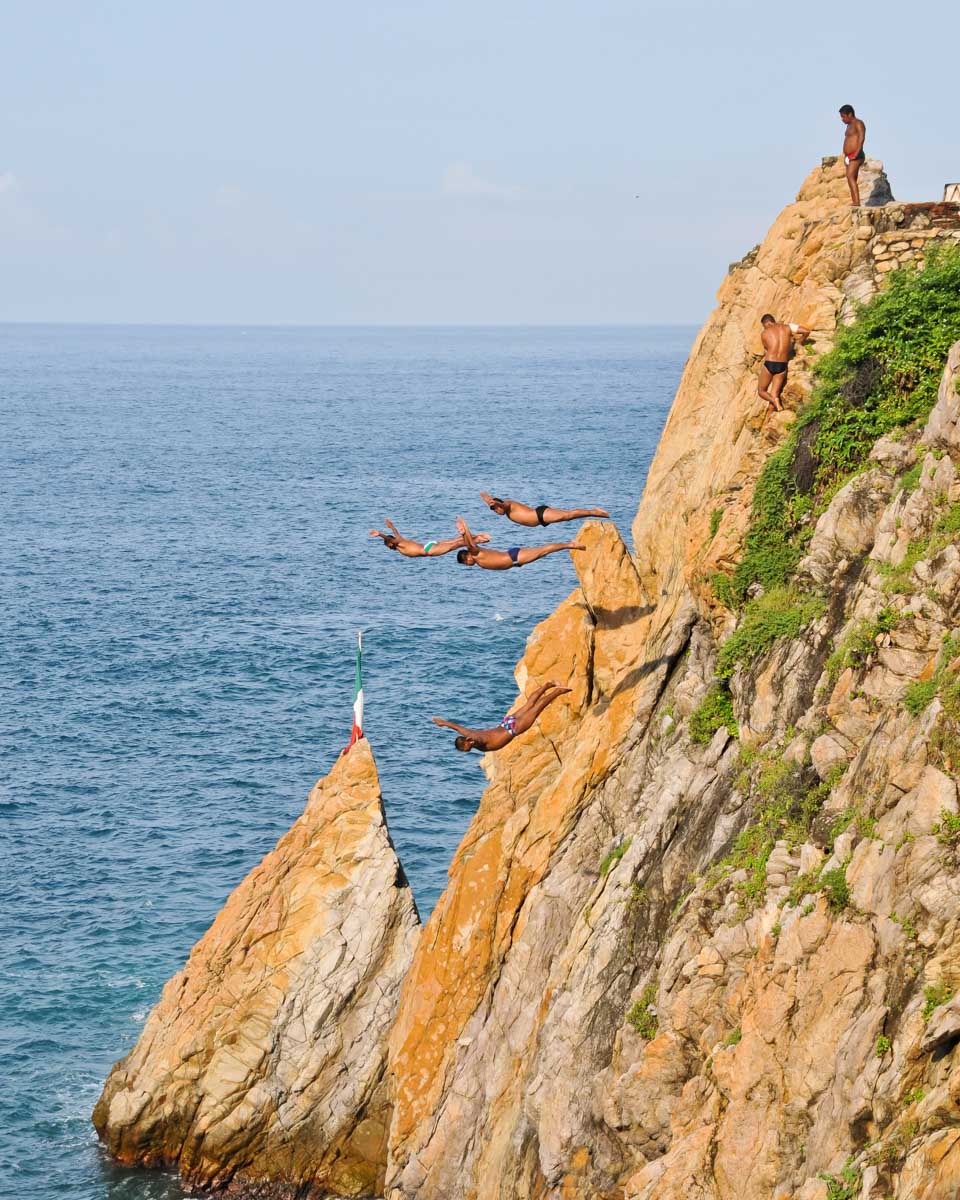 Three men dive from a cliff in Acapulco at the La Quebrada Diving platforms