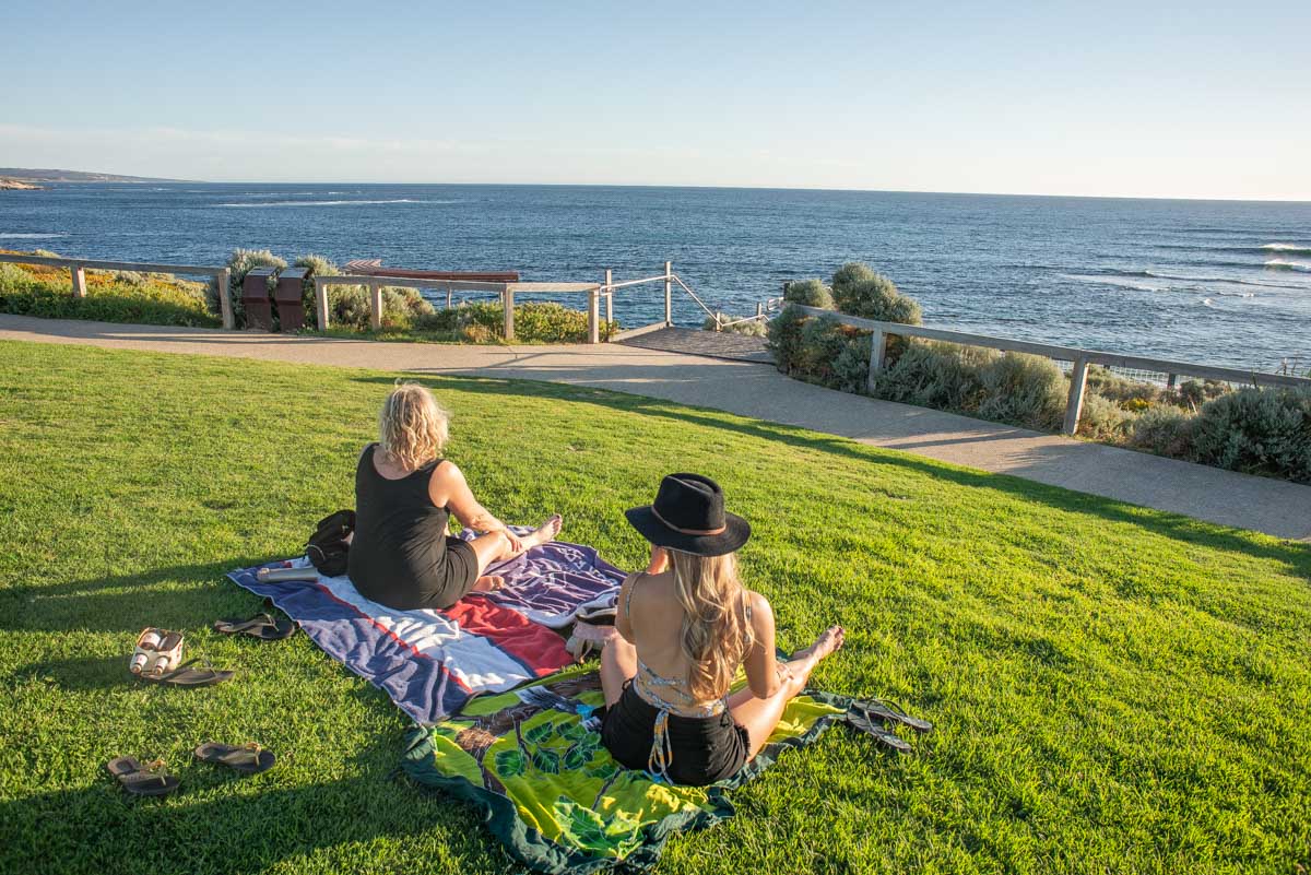 Two people watch the sunset on the grass at Surfers Point in Margaret River, Western Australia