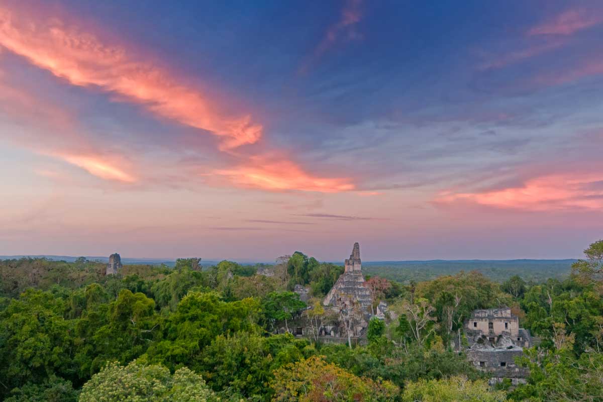 Sunset at Tikal, Guatemala with views of the temples poking through the trees