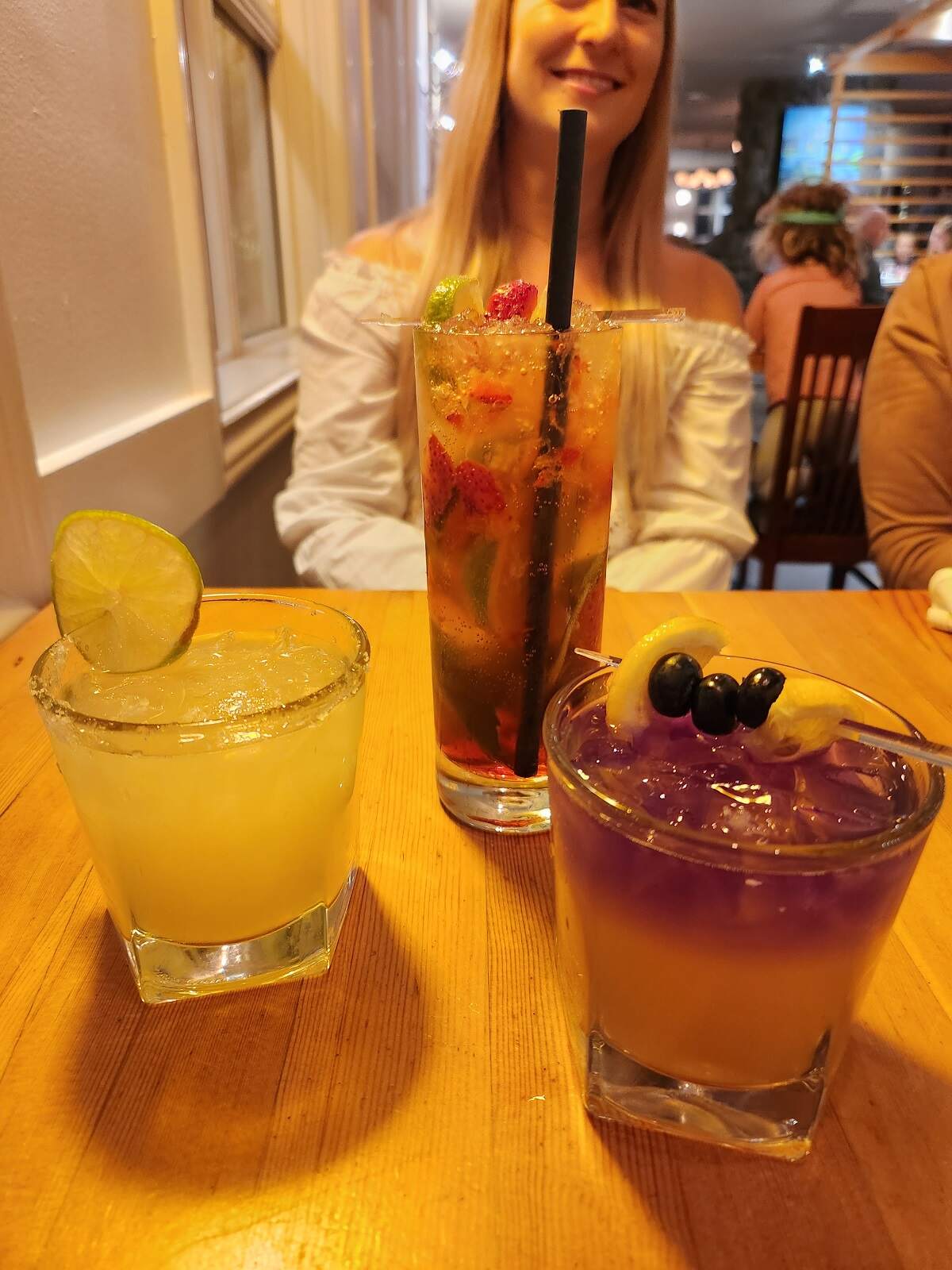 Bailey sits at a table with three craft cocktails in front of her