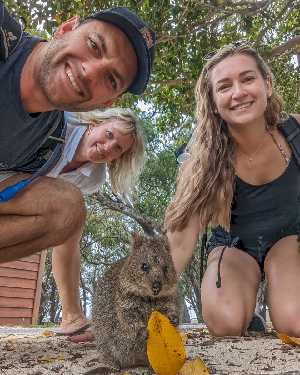 Three people take a selfie with a quokka on Rottnest Island, Perth, WA