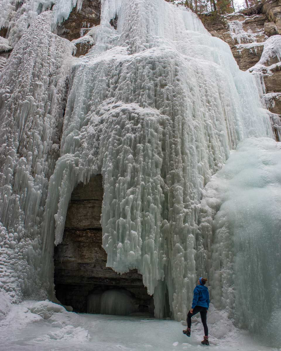 A lady looks up at a frozen waterfall in Maligne Canyon