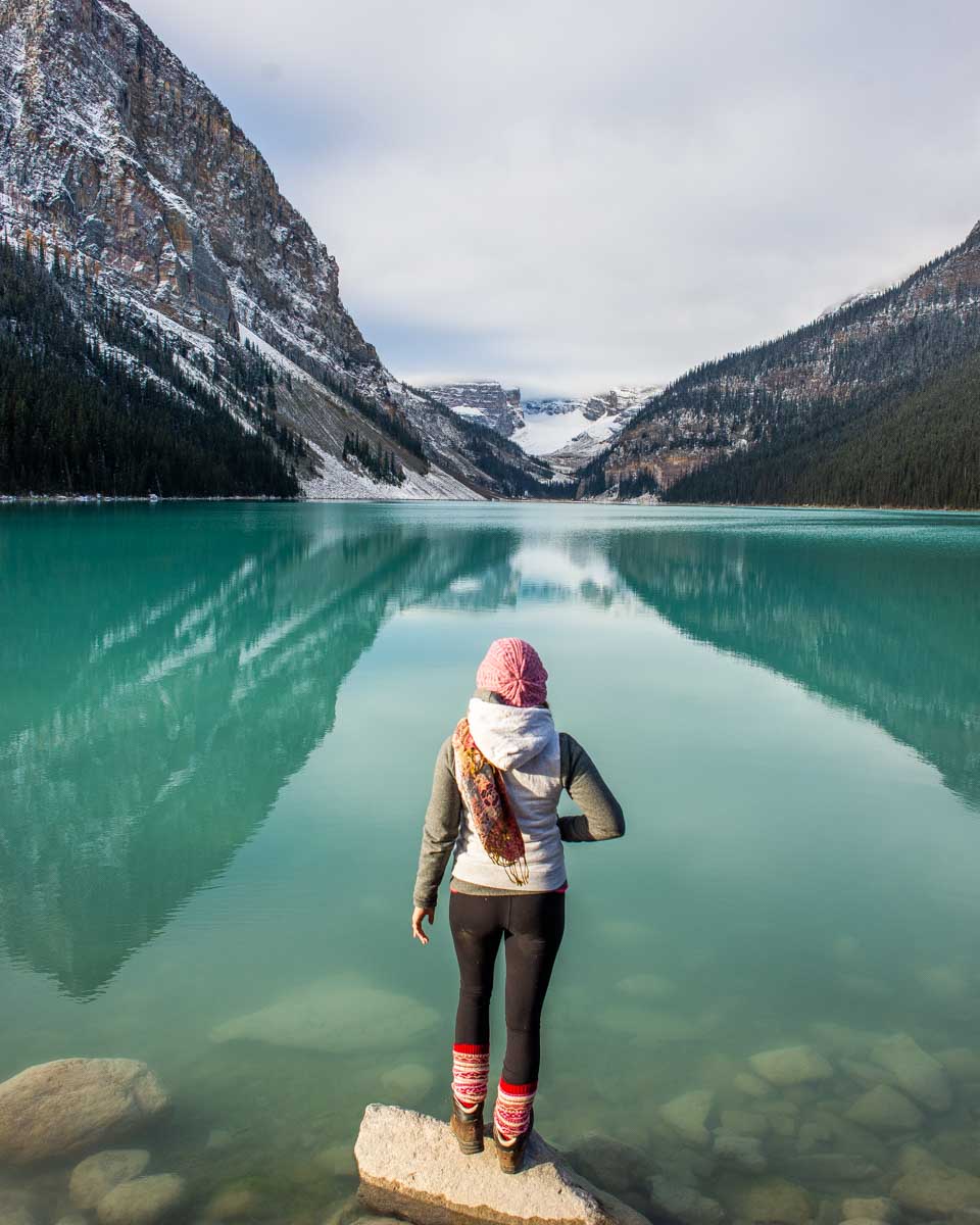woman stands on the edge of the calm Lake Louise