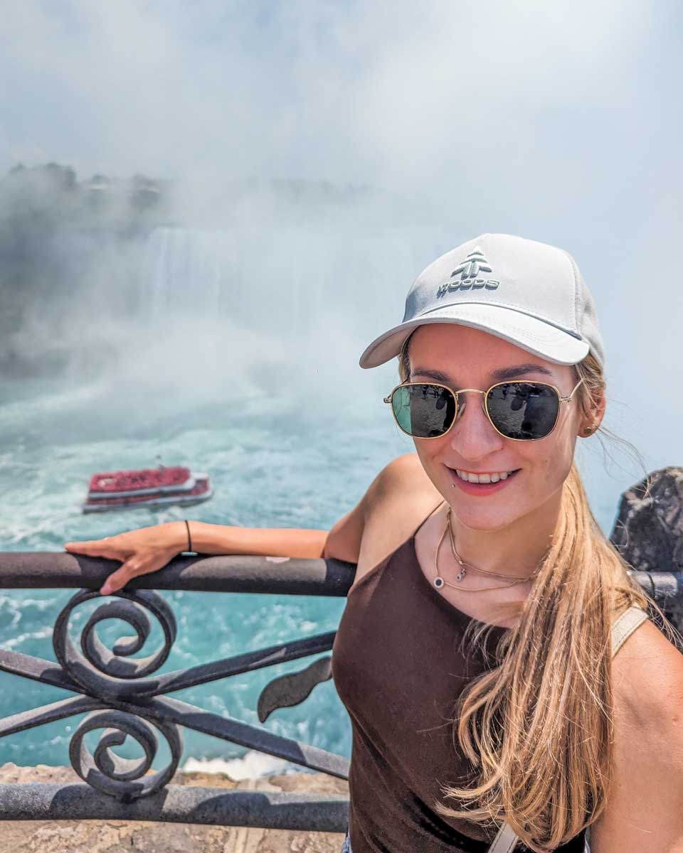 Bailey leans on the railing on the Canadian side of Niagara Falls as a cruise heads towards the falls below her