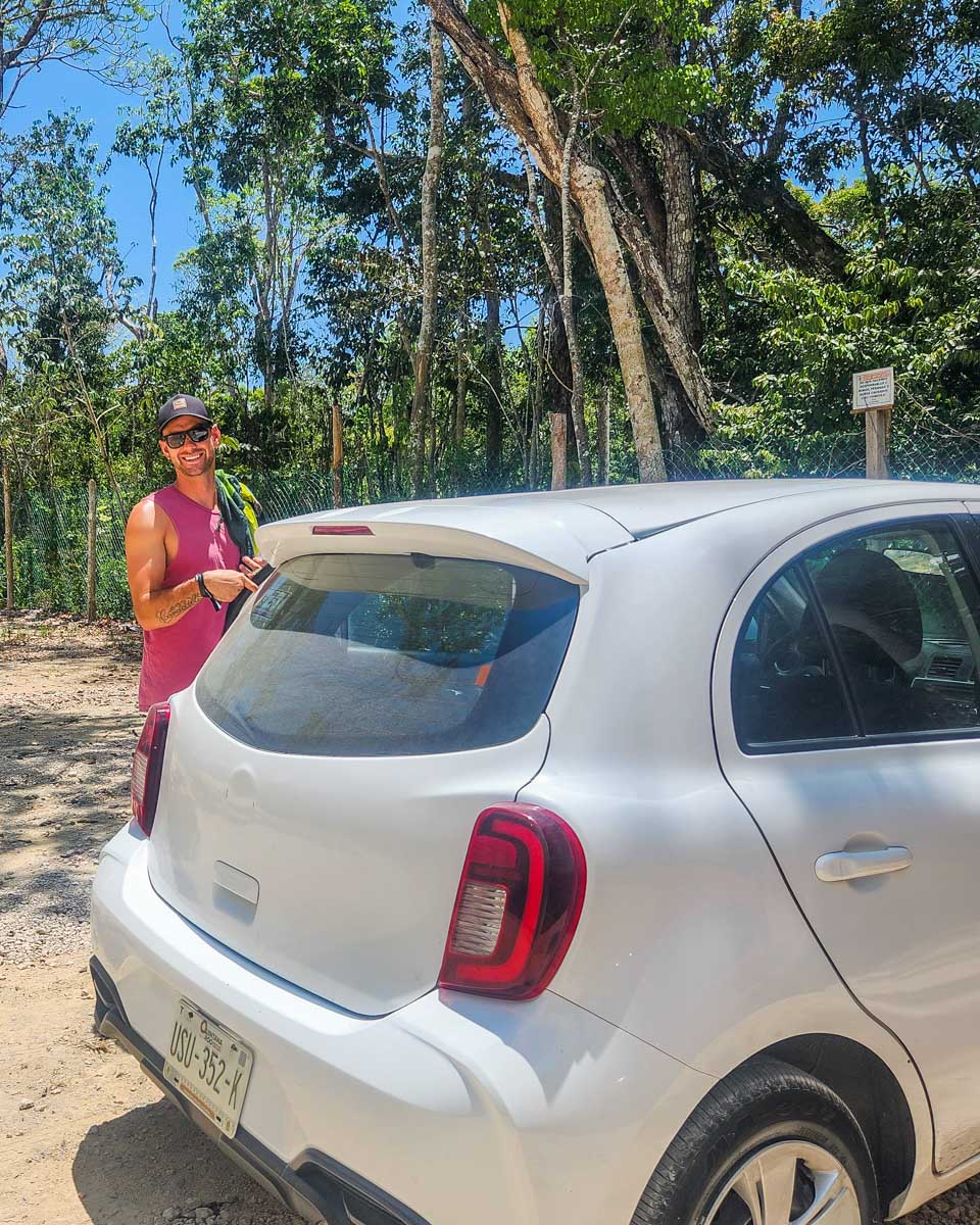 Daniel poses for a photo with our rental car at a cenote in tulum, Mexico