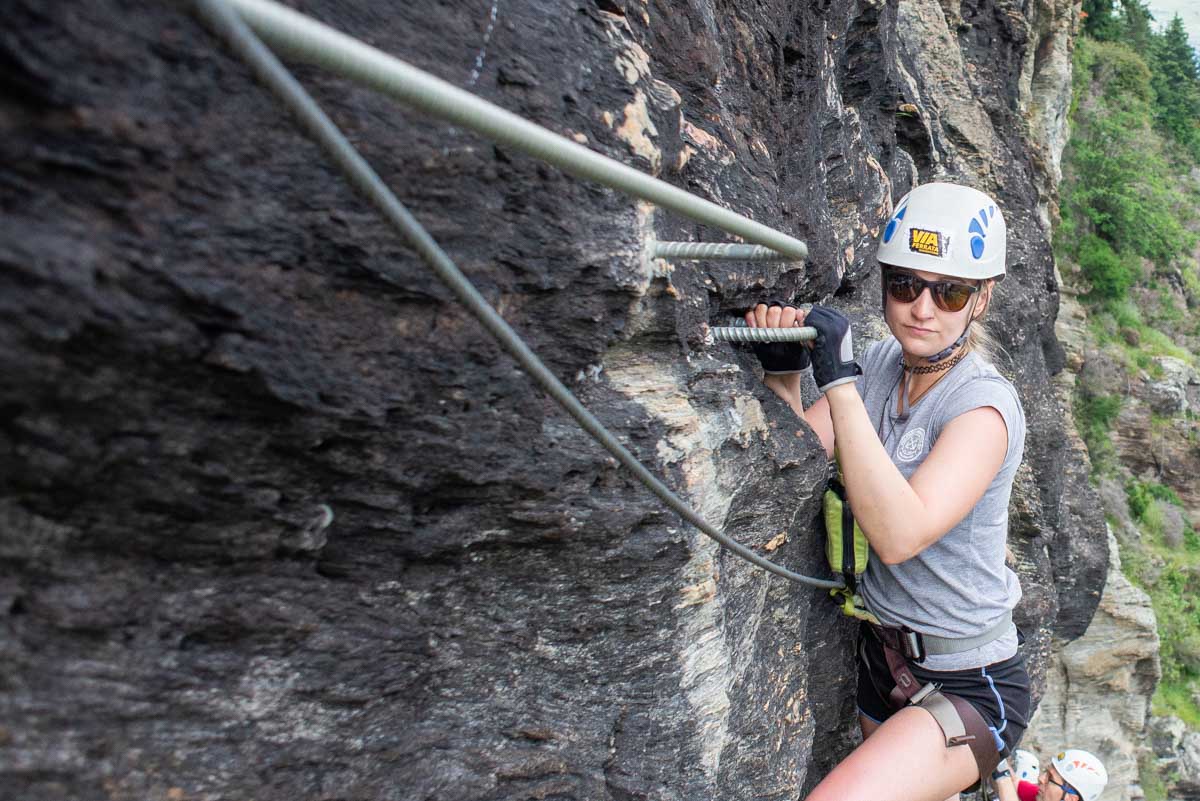 bailey hangs on a cliff while trying via ferrata