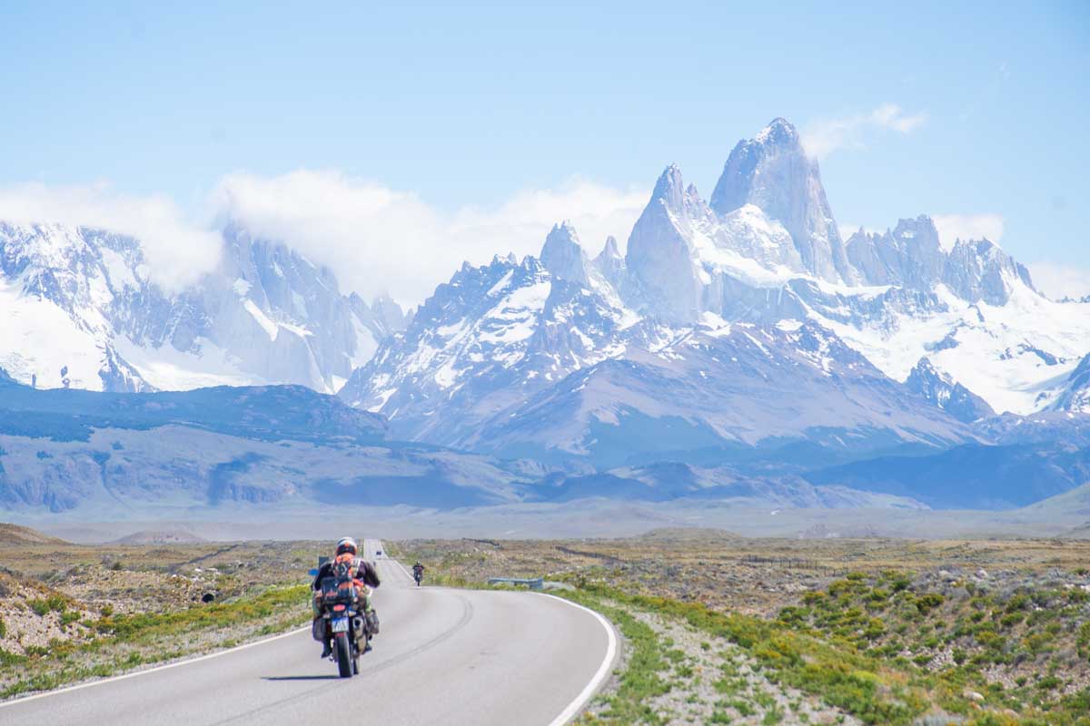 A motorcycle drives along a road into El Chalten with a mountain backdrop in Argentina