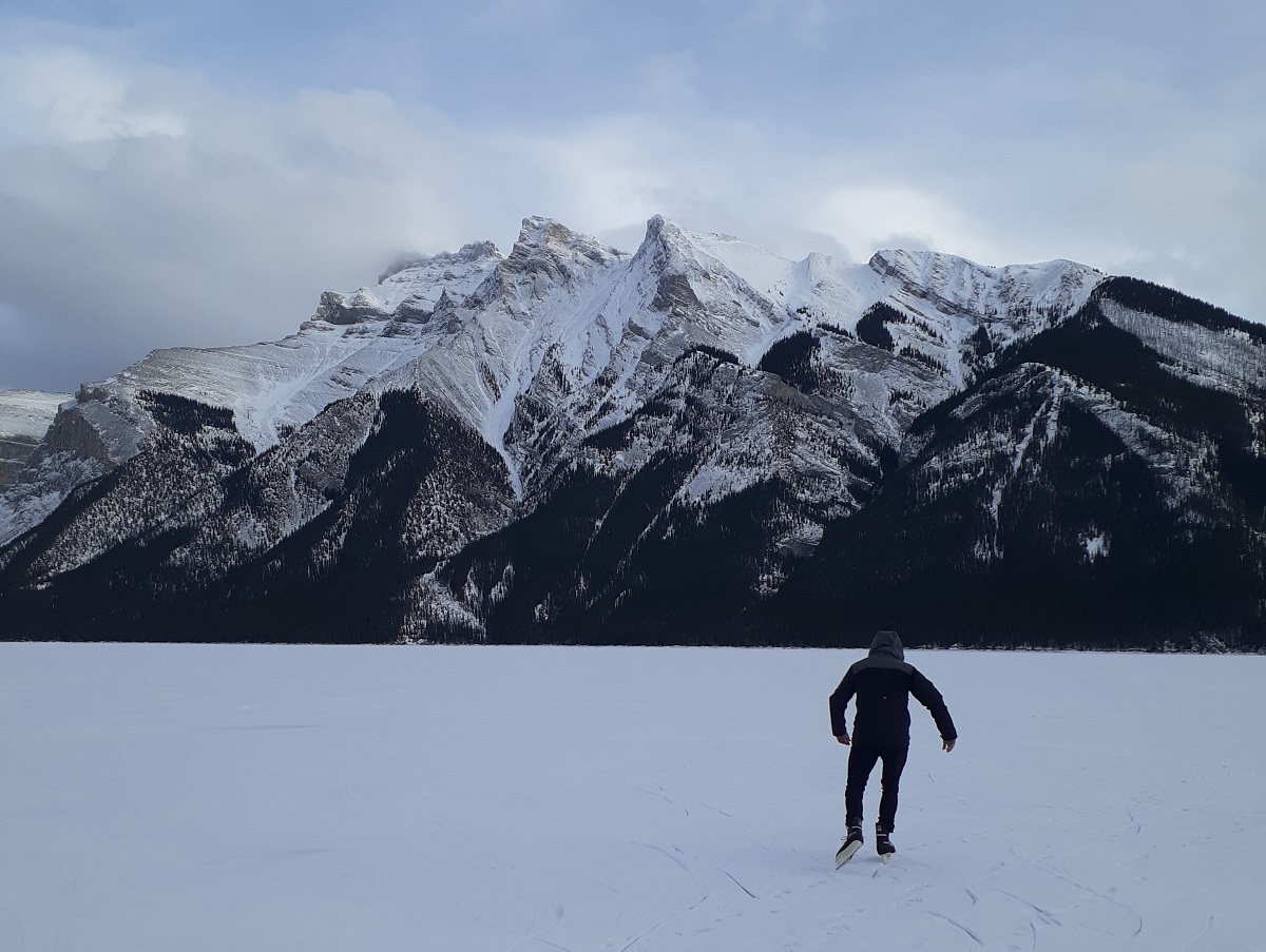 Daniel skates on the snow covered Lake Minnewanka with mountains in the background