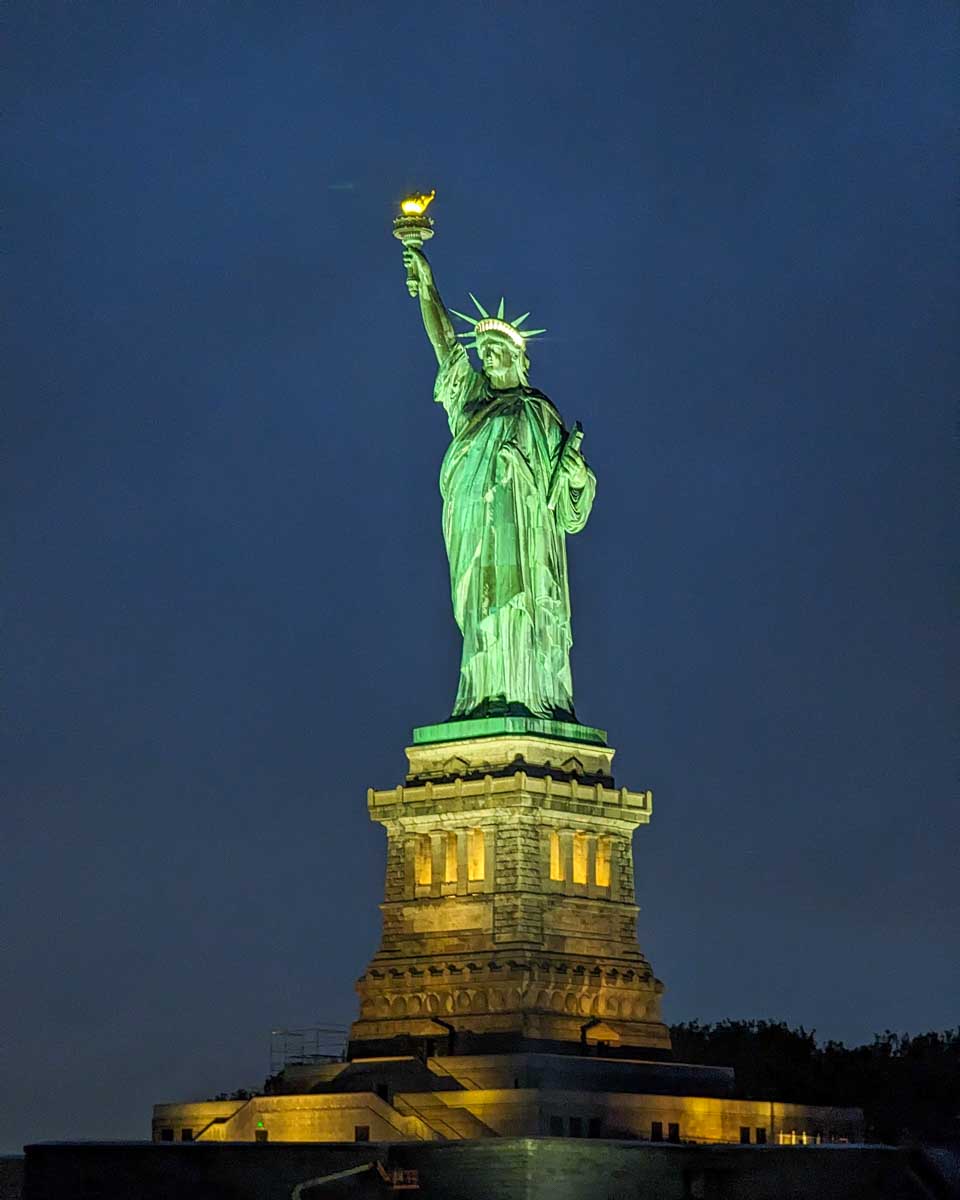 The Statue of Liberty lit up at night as seen from a dinner cruise in New York City
