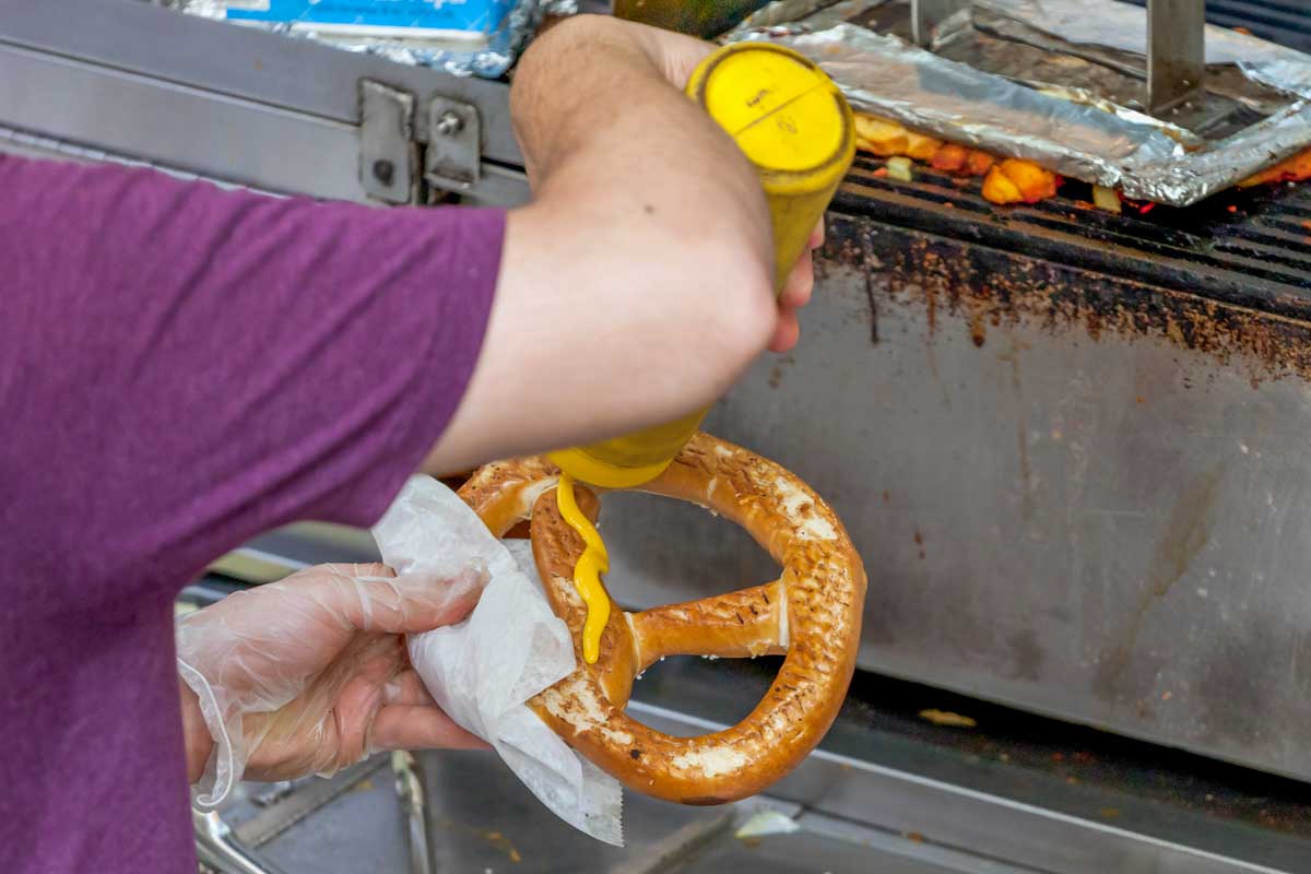 A man puts mustard on a pretzel in NYC