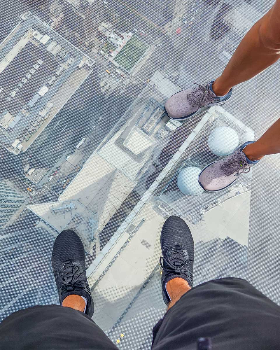 Two people stand on the glass floor at the Edge NYC Observation deck
