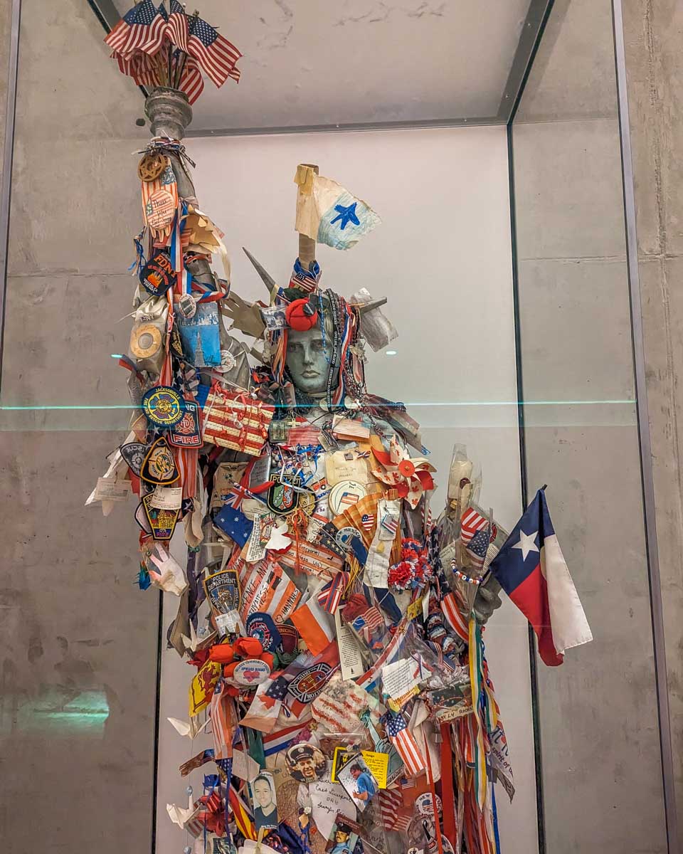 A small statue of the statue of Liberty covered in flags, badges etc