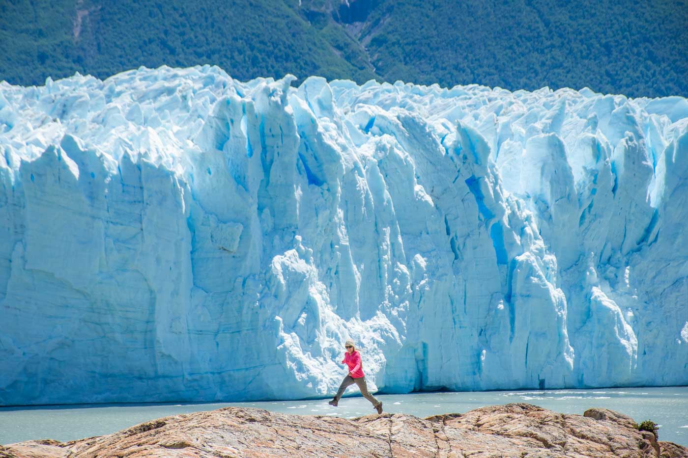 A lady jumps between rocks with Perito Moreno Glacier in the background