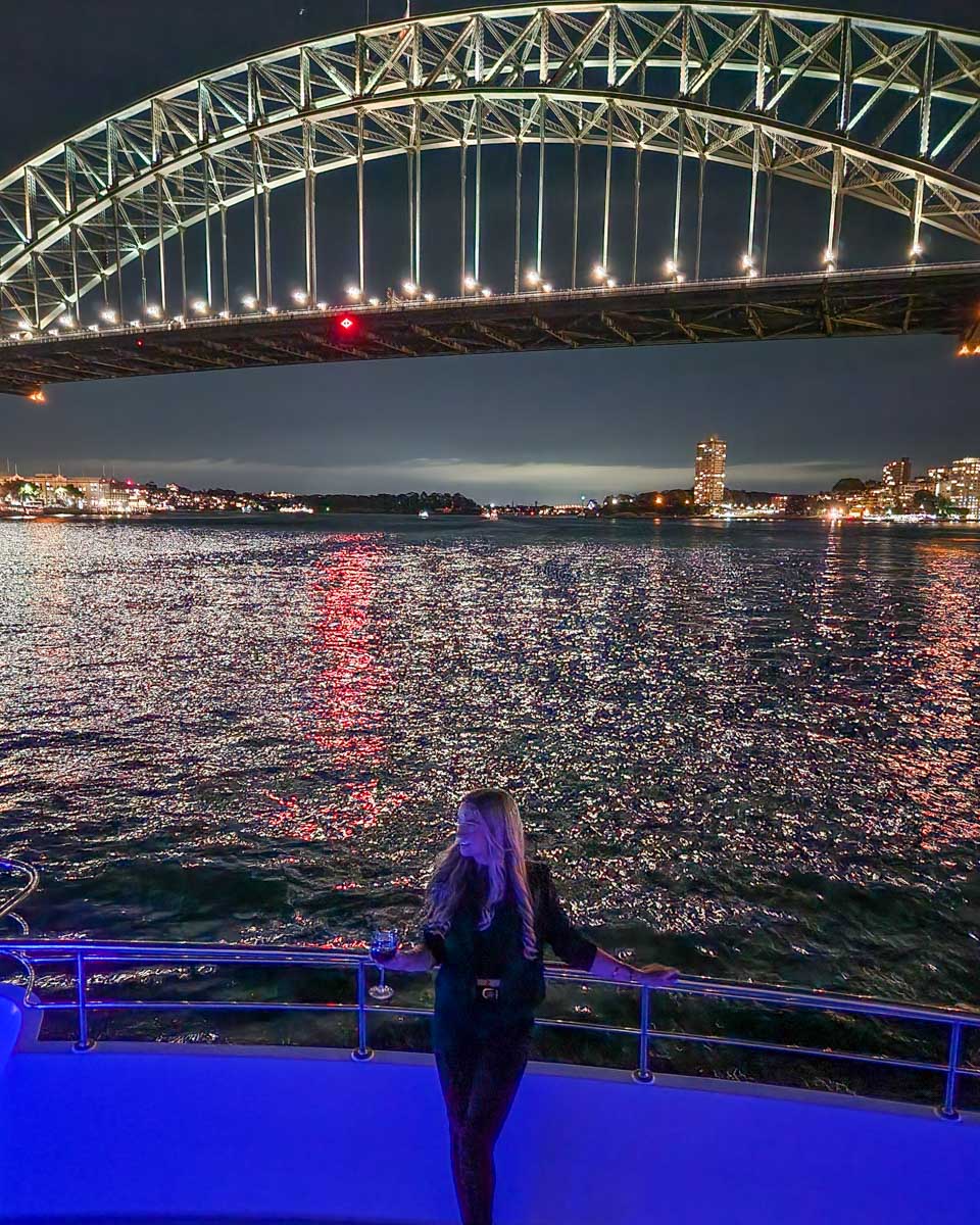 Bailey stands at the front of the boat with views of the Sydney Harbour Bridge on a dinner cruise