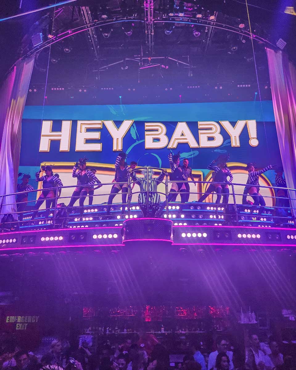 Dancers on an upper stage dance with a sign above them that says hey baby